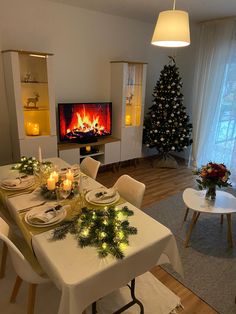 a dining room table set for christmas dinner with lit candles and decorated tree in the background