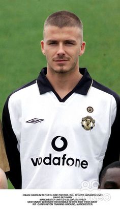 a man standing in front of a soccer field holding a baseball bat and wearing a black and white shirt