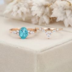 two gold rings with turquoise stones and diamonds on them sitting on a white box next to flowers