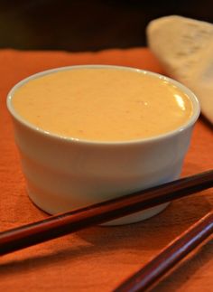 two chopsticks sit next to a bowl of soup on an orange cloth with a towel in the background