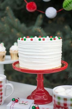 a white frosted cake sitting on top of a table next to cupcakes