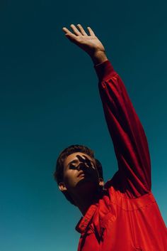 a man in a red shirt reaching up into the air to catch a frisbee