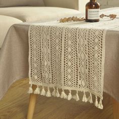 a table topped with a bottle of wine and tasselled doily on top of a wooden table