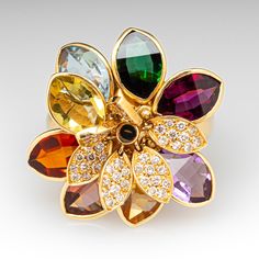 This playful Vianna Brazil designed ring features a floral design featuring eight (8) gemstones, in articulating bezel settings. Atop the colored gemstones are six (6) articulating petals, each bead set with ten (10) round brilliant cut diamonds. The ring measures 25.3mm at the top, rises 8.7mm above the finger, and tapers to 3.2mm wide by 1.0mm thick at the base of the shank. The ring is crafted in 18k yellow gold and is currently a size 9.25. Multicolor Cluster Jewelry For Formal Occasions, Multicolor Cluster Fine Jewelry, Elegant Multicolor Cluster Jewelry, Formal Multi-stone Yellow Gold Flower Ring, Multicolor Cluster Jewelry With Accent Stones, Flower-shaped Multi-stone Wedding Jewelry, Flower Shaped Multi-stone Wedding Jewelry, Elegant Multicolor Flower-shaped Rings, Fine Jewelry Flower-shaped Multi-stone Rings