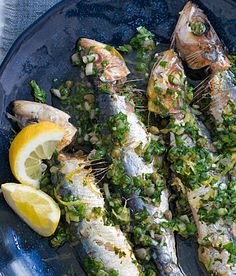 some fish are on a blue plate with lemon wedges and garnishes