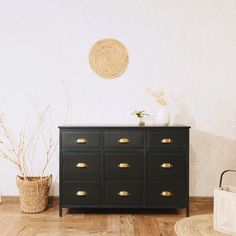 a black dresser with gold handles in a white room next to a basket and plant