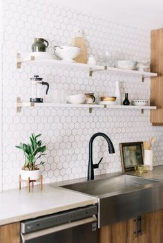 a kitchen with white hexagonal tiles on the wall and shelving above the sink