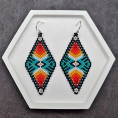 These geometric beaded earrings, crafted from my original design, showcase a vibrant blend of turquoise and black with intricate patterns. The diamond-shaped design is accented by a striking gradient that transitions from rich reds and oranges to bright yellows, with white X-shaped patterns at the center. Subtle touches of gold bring an added element of sophistication. Perfect for adding a colorful Southwestern flair to your outfit, these earrings are versatile enough to pair with both casual an Southwestern Multicolor Teardrop Beaded Earrings, Colorful Beaded Southwestern Earrings For Festival, Southwestern Colorful Beaded Earrings For Festivals, Handmade Multicolor Geometric Jewelry, Handmade Geometric Multicolor Jewelry, Southwestern Style Colorful Beaded Earrings, Southwestern Multicolor Beaded Earrings, Multicolor Beaded Geometric Earrings, Native American Beaded Earrings Inspire Uplift ⭐