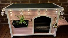 a small dog house with lights on and a plant in the front window, sitting on a wooden floor next to a brick wall