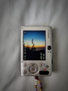 a white cell phone sitting on top of a bed next to a beaded bracelet