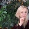 a woman sitting in front of a plant with her hand on her chin and looking at the camera