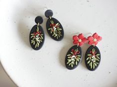 three black and red earrings with flowers on them sitting on a white plate next to each other