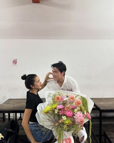 a man kneeling down next to a woman holding a bunch of flowers in front of her