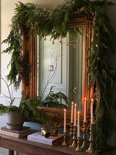 a mirror and some candles on a table in front of a mirror with greenery