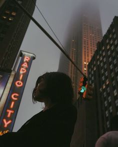 a woman standing in the middle of a street next to tall buildings and traffic lights