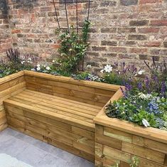 a wooden bench sitting next to a brick wall and flower garden planter filled with flowers