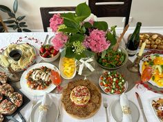 a table topped with lots of plates and bowls filled with food next to wine bottles