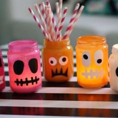 four jars with candles decorated to look like skulls and faces, one has candy sticks sticking out of it