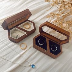 two wooden jewelry boxes with rings and necklaces in them on a white cloth covered bed