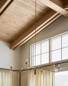 a kitchen with wooden ceiling and white curtains on the window sill, along with two hanging lights