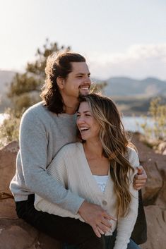 a man and woman hugging each other while sitting on rocks