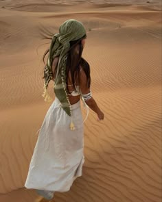 a woman is walking in the desert wearing a white dress and green headdress