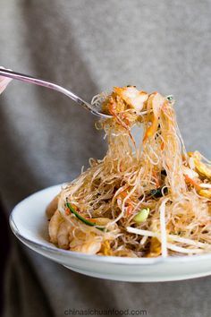 a person holding a white plate with noodles and vegetables on it while eating from a fork