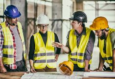 three men in safety vests and hard hats looking at blueprint on a table