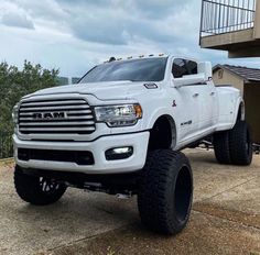 a white ram truck parked in front of a building with large tires on it's tires