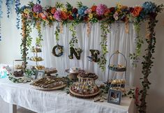 a table topped with cakes and desserts under a floral covered wall hanging from the ceiling