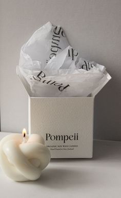 a white candle sitting in front of a box with some paper on top of it