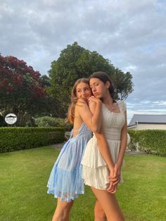 two young women standing next to each other in the grass