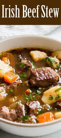 a bowl of beef stew with potatoes and carrots in it on a white table