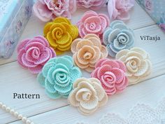 small crocheted flowers sitting on top of a white wooden table next to pink roses