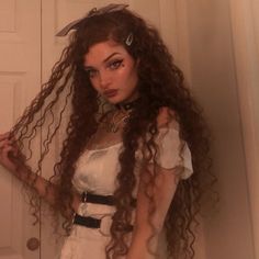 a woman with long curly hair standing in front of a door wearing a white dress