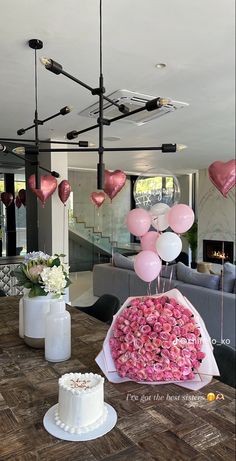 a table topped with a white cake and lots of pink balloons in the shape of hearts