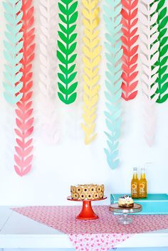 colorful paper leaves are hanging on the wall above a table with cake and drinks in front of it