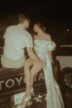 a man sitting on the back of a truck next to a woman in a white dress