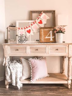 a wooden table topped with lots of pillows next to a white dresser covered in valentine's day decorations