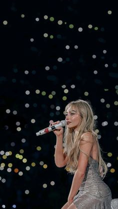 a woman in a silver dress is holding a microphone and singing into the air with confetti all around her