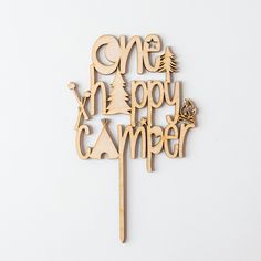 a wooden cake topper with the words one happy camper written in cursive writing