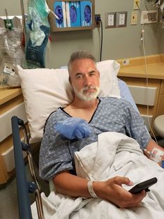 a man laying in a hospital bed holding a remote control