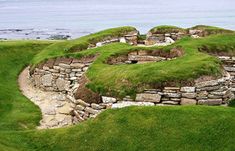 an old stone structure with grass growing on it's sides and water in the background