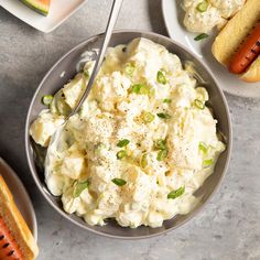 a bowl filled with mashed potatoes next to hot dogs