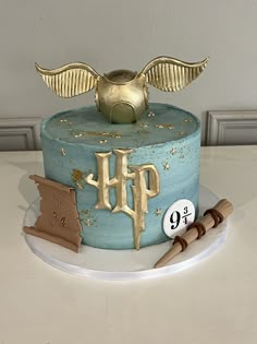 a blue cake with gold decorations and an angel's wing on top is sitting on a table