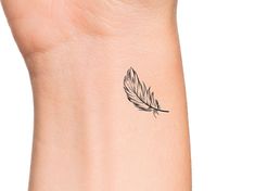 a small feather tattoo on the wrist is shown in black and grey ink, with an outline of a bird's wing