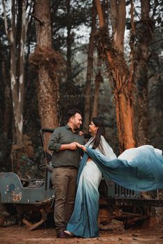 a man and woman standing next to each other in the woods with a blue blanket draped over them