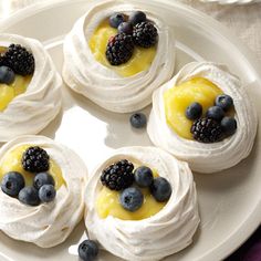 small desserts are arranged on a plate with berries and blueberries in the center