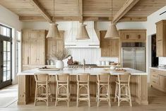 a large kitchen with lots of counter space and wooden accents on the ceiling, along with bar stools