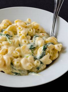 a white plate topped with pasta and spinach covered in sauce next to a fork